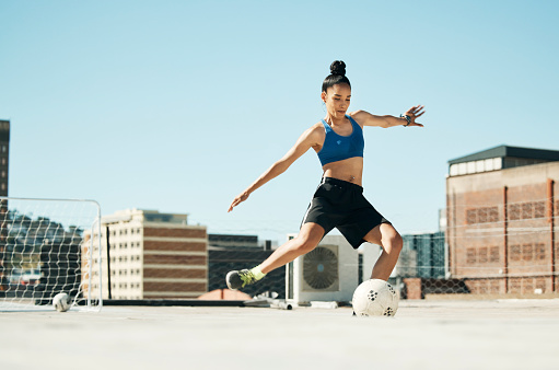 Soccer player, woman and soccer ball kick in fitness, training or exercise on Portugal city building rooftop. Football player, sports person and athlete in energy workout for health or wellness goals