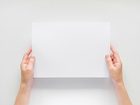 female hands hold an empty white sheet of A4 paper on the background of a white table. empty space for text