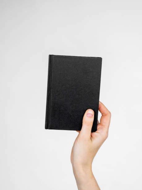 istock female hand holds a notebook or a book with an empty black cover. space and template for text 1446528585