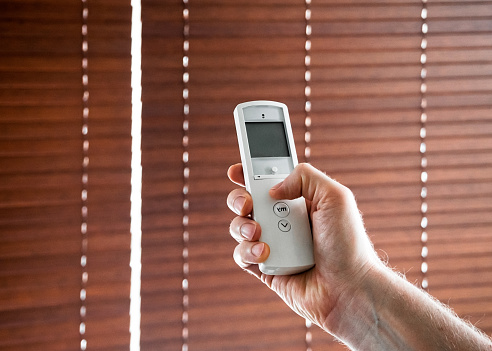 male hand holds a remote control to open the window blinds