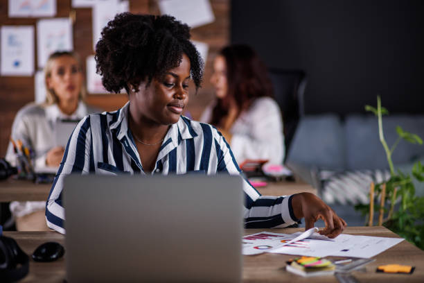 istock Charming Black businesswoman writing notes and using laptop when working at her desk 1446528660