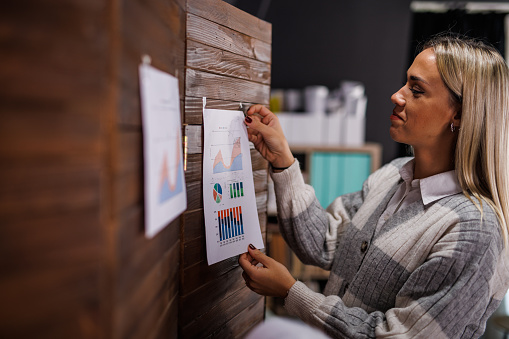 Portrait of creative young woman hanging a color chart on the wall in her office while working on a project.