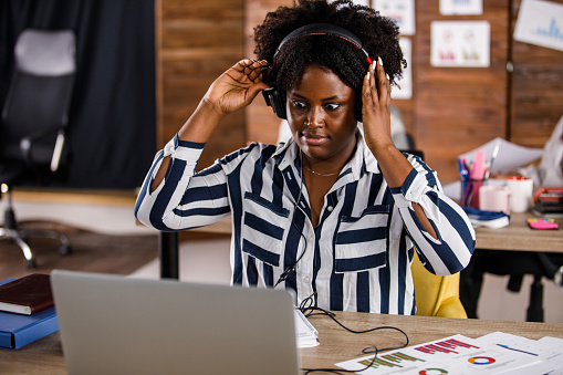 Candid shot of shocked young woman sitting at her desk at the office and putting on headphones when joining a video conference call and being late.