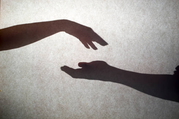 istock Grey shadows of hands reaching each other on the wall. Abstract blurred effect with space for text. 1446530855