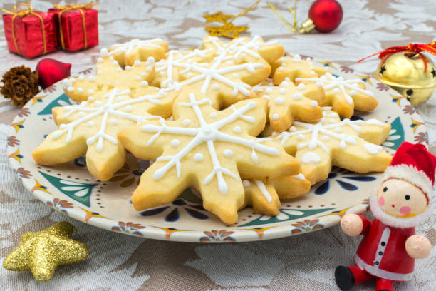 Snowflake-shaped Christmas sugar icing cookies, on a tablecloth and some Christmas decoration
