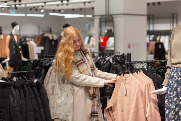 Young female customer with golden hair choosing clothes in modern women cloths store. Young female customer with golden hair choosing clothes in modern women cloths store. Shopping concept. young hot stock pictures, royalty-free photos & images