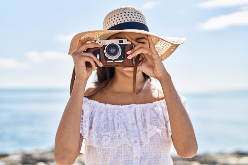 Young african american woman tourist smiling confident using camera at seaside