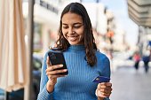Young african american woman using smartphone and credit card at street