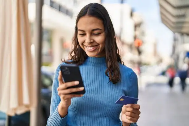 Photo of Young african american woman using smartphone and credit card at street