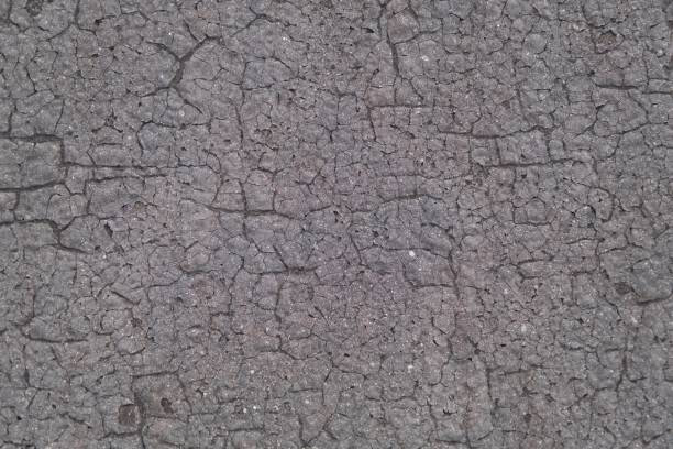 Weathered old dark gray ruberoid texture with numerous cracks and fractures, sun-scorched surface for use as a background.