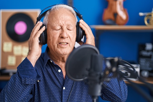Senior grey-haired man artist singing song at music studio