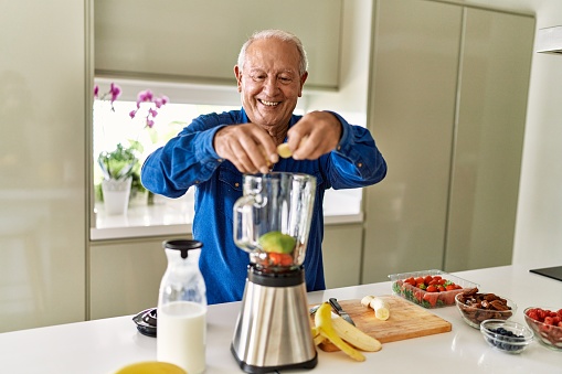 Senior man smiling confident putting banana in blender at kitchen