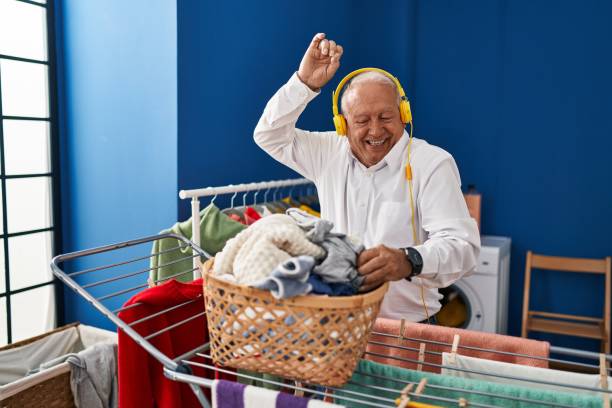 hombre mayor escuchando música colgando ropa en el tendedero en la lavandería - all laundry detergent audio fotografías e imágenes de stock