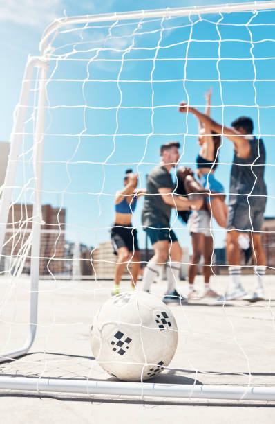 football, soccer team and ball in goal post or net with diversity sports group of men and women in celebration of win, winning and scoring on urban rooftop. exercise, concrete training and champions - soccer celebration success group of people imagens e fotografias de stock