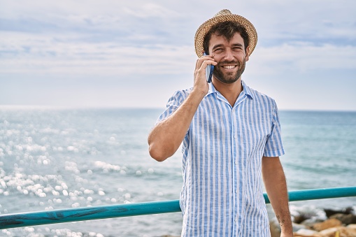 Young hispanic man smiling happy talking on the smartphone at the beach