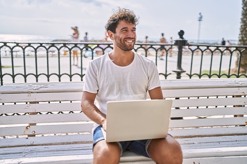 Young hispanic man smiling confident using laptop at seaside