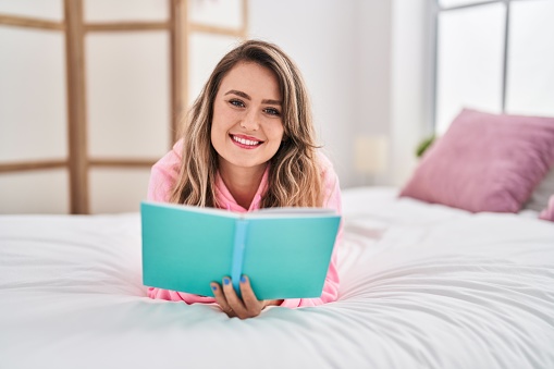 Young woman reading book lying on bed at bedroom