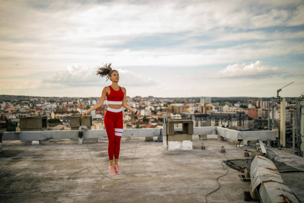 Attractive young woman jumping skipping rope outdoors on building rooftop in city in urban area. She is wearing sports clothing and looks very fit and healthy