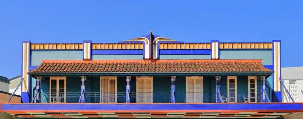 Flat parapet of AD1941 Spanish Mission Art Deco style building on Rankin Street-suspended first floor balcony with tiled roof on fanciful Egyptian papyrus capitals-cast iron railing. Innisfail-QLD-AUS