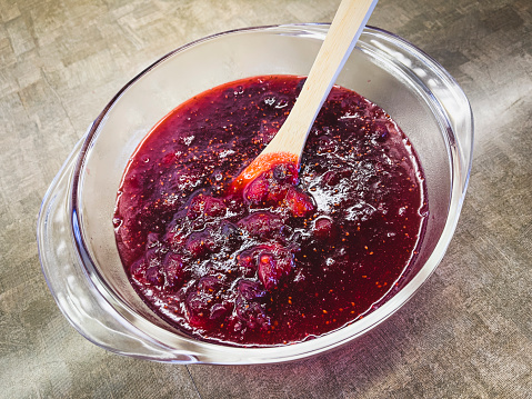 A glass bowl of freshly prepared cranberry sauce with a wooden spoon. Cranberry sauce is traditionally served as a side dish at Thanksgiving and Christmas. Taken on a mobile device.