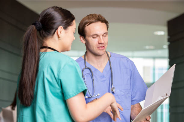 Mid adult man is nurse in busy hospital and is speaking with coworker about patient care stock photo