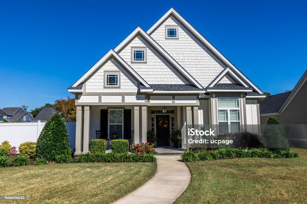 The front view of a cottage craftsman style white house with a triple pitched roof with a sidewalk, landscaping and curb appeal The front view of a new construction cottage craftsman style white house with a triple pitched roof with a sidewalk, landscaping and curb appeal. House Stock Photo