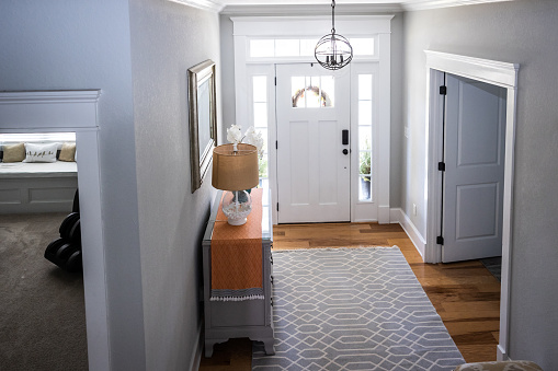 An open large and wide interior front door hallway foyer with transom, hanging light fixture, coastal colors and entry way table and wood floors taken from a high angle.