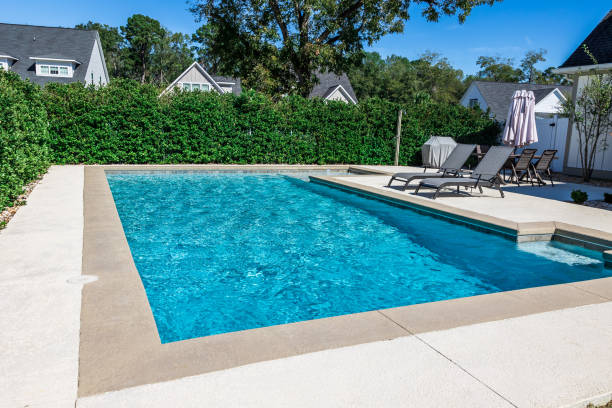 a rectangular new swimming pool with tan concrete edges in the fenced backyard of a new construction house - yüzme havuzu stok fotoğraflar ve resimler