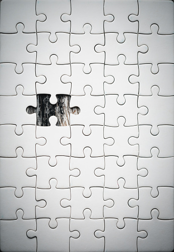 Unfinished blue puzzle with last one piece on white table background. Closeup. Wide banner. Empty place for text. Top down view.