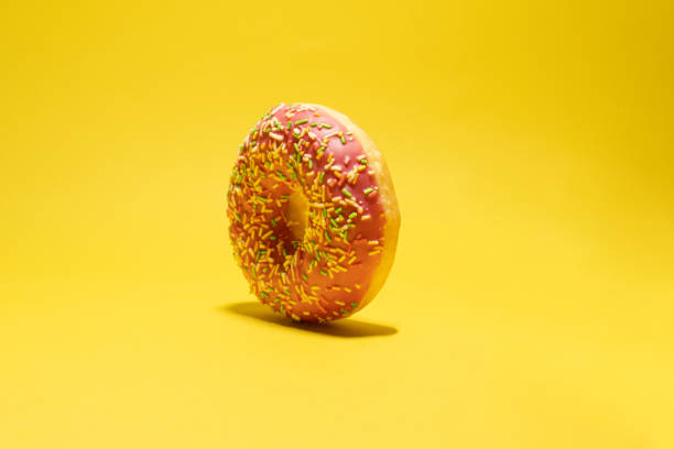 istock Pink donut with multicolored sprinkles on yellow background. Creative food background 1446558728