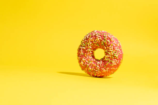 istock Pink donut with multicolored sprinkles on yellow background. Creative food background 1446558731
