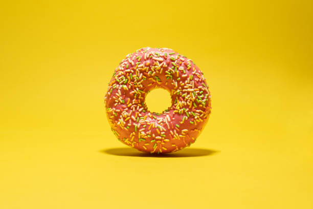 istock Pink donut with multicolored sprinkles on yellow background. Creative food background 1446558734