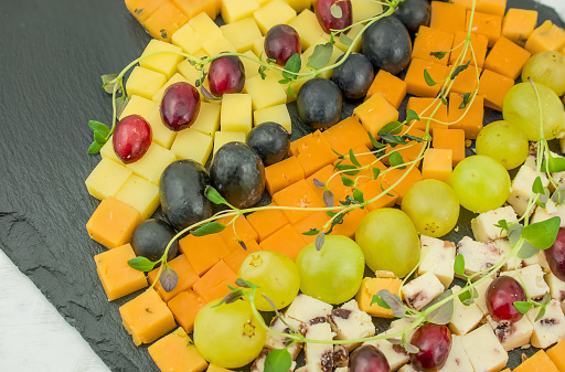 Various types of cheese on black board with grapes