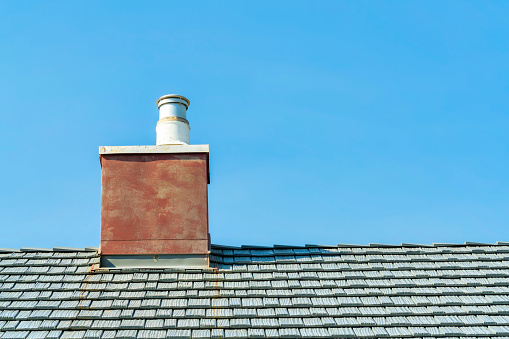 red chimney with metal vent and gray roof on blue sky background in sun midday or late afternoon