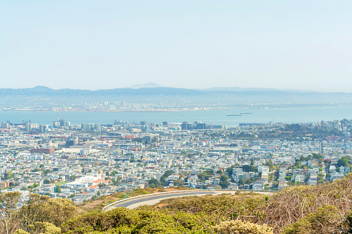 winding hillside road and hill in foreground with sunlit city downtown san francisco and neighborhoods with ocean and mountain background midday no shade