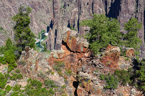 An overview of a narrow section of the Black Canyon with rocks in the foreground and the Gunnison River far below flanked by steep cliffs.