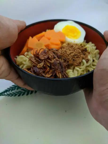 Photo of a bowl of noodles with some garnishes is in hand