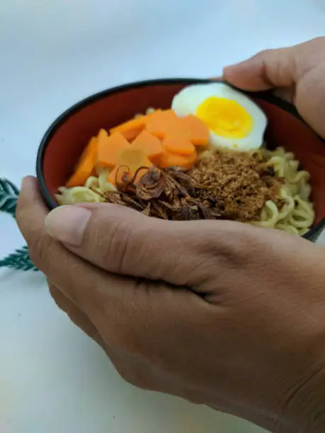 Photo of a bowl of noodles with some decorations carried in two hands