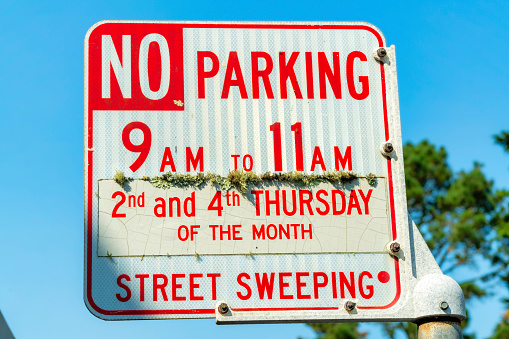 No parking sign from nine to eleven for street sweeping in urban or suburban area with foliage and tree with blue sky background. Late afternoon or early morning in partial sun and no clouds.