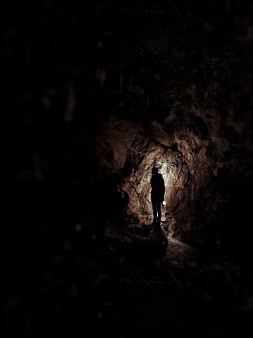 A man stops inside the dark cave, his flickering lantern the only source of light.