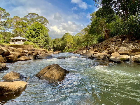 Horizontal landscape of flowing creek waters through rock lined riverbed with tree background in public parks at Bangalow Australia