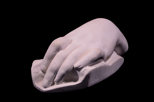 A closeup shot of a white handmade hand clay statue isolated on a black background