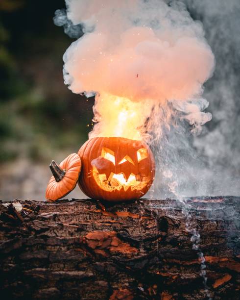 istock Vertical closeup of a lighting up pumpkin on a tree trunk smoke coming from head blurred background 1446619929