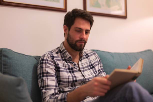 istock Caucasian man sitting on a sofa and reading a book. 1446620814