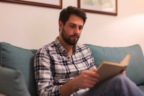 istock Caucasian man sitting on a sofa and reading a book. 1446620917