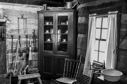 A grayscale of an old rustic house filled with antique pieces of equipment
