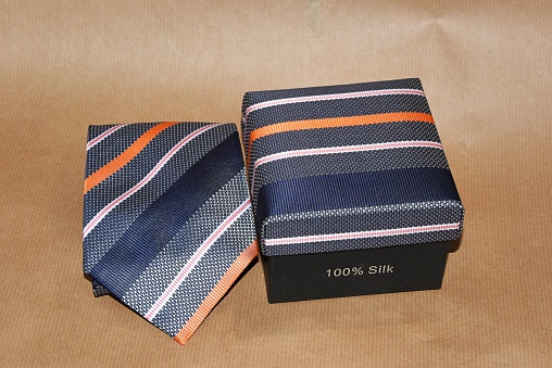 A close-up of a regimental stripe silk necktie with its box, isolated on a beige background