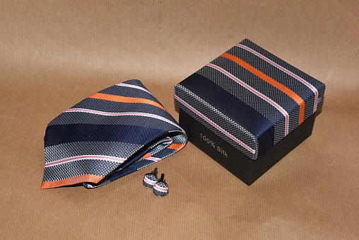 A close-up of a regimental stripe silk necktie, cufflinks and a box and isolated on a beige background