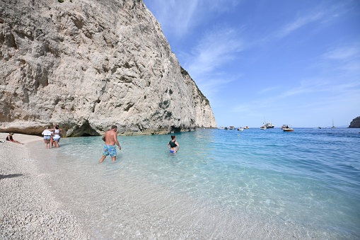 zakyntos, Greece – May 07, 2022: A beach with people swimming and boats sailing next to a big cliff