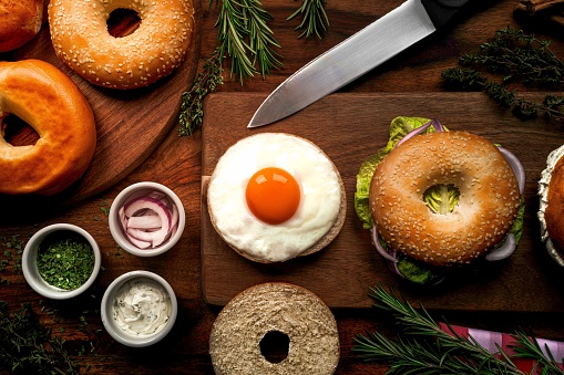 A top view of a bagel sandwich with egg and other ingredients on a wooden cutting board